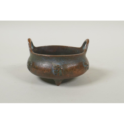 181 - A Chinese bronze two handled censer on tripod supports, with raised character decoration, impressed ... 