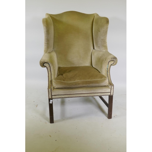 1175 - A Georgian style wing back armchair with brass stud decoration, raised on square mahogany supports