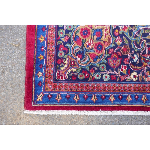 1010 - A rich red ground vintage Persian Mashad carpet with traditional floral medallion with signature of ... 