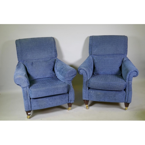 1065 - A pair of contemporary easy chairs, raised on turned mahogany supports with brass castors