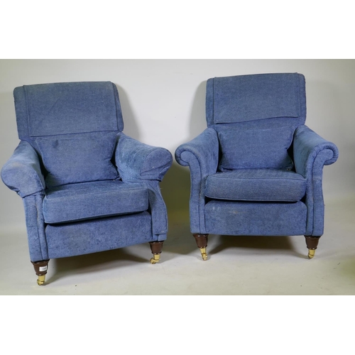 1065 - A pair of contemporary easy chairs, raised on turned mahogany supports with brass castors