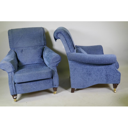 1065 - A pair of contemporary easy chairs, raised on turned mahogany supports with brass castors