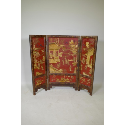 1083 - A C19th Chinese export three fold red lacquered fire screen with raised gilt chinoiserie decoration,... 