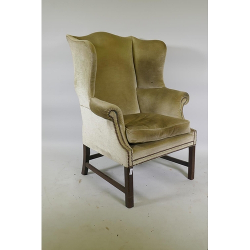 1175 - A Georgian style wing back armchair with brass stud decoration, raised on square mahogany supports