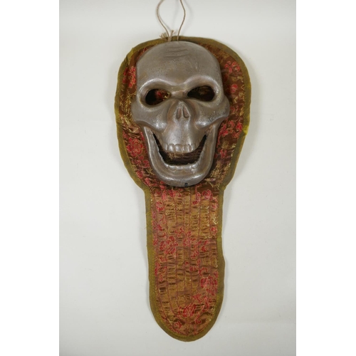 178 - A Tibetan white metal citipati death mask on a silk mount, 45cm long