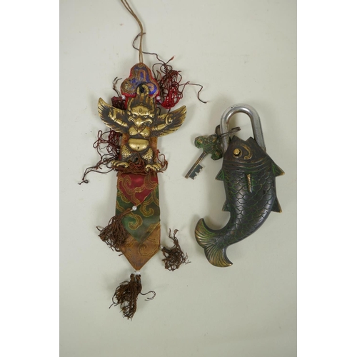 59 - A Tibetan bronze Garuda amulet on a silk mount, and a bronze carp shaped padlock, 23cm long