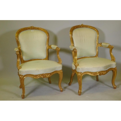 1001 - A pair of antique watergilt show frame armchairs with carved decoration and silk covers, raised on c... 