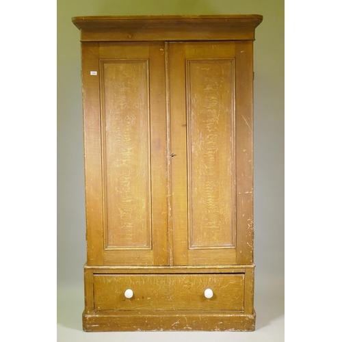 1033 - A Victorian grain painted pine wardrobe, with two doors over a single drawer, raised on a plinth bas... 