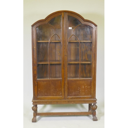 1080 - A 1930s oak dome top display cabinet/bookcase, two glazed doors with arched glazing bars, raised on ... 