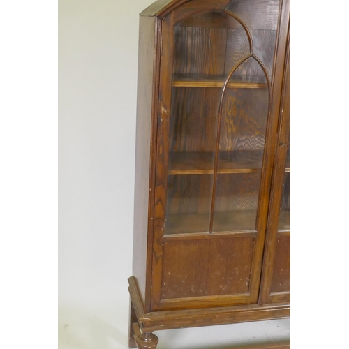 1080 - A 1930s oak dome top display cabinet/bookcase, two glazed doors with arched glazing bars, raised on ... 