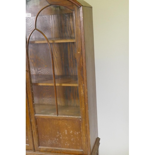 1080 - A 1930s oak dome top display cabinet/bookcase, two glazed doors with arched glazing bars, raised on ... 