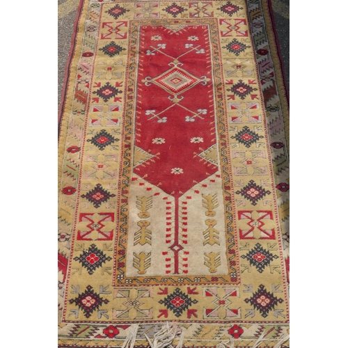 1225 - A Middle Eastern wool carpet with red central panel and gold coloured borders with geometric designs... 