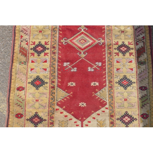 1225 - A Middle Eastern wool carpet with red central panel and gold coloured borders with geometric designs... 