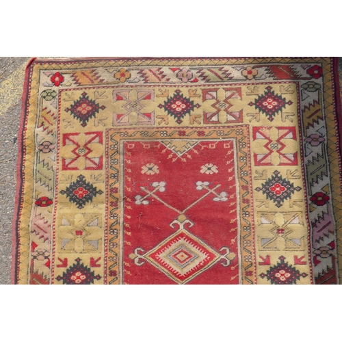 1225 - A Middle Eastern wool carpet with red central panel and gold coloured borders with geometric designs... 