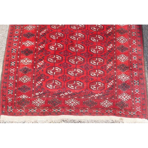 1226 - A vintage Bokhara wool rug with traditional design on a red field, 115 x 146cm