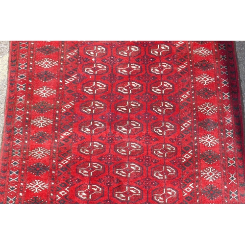 1226 - A vintage Bokhara wool rug with traditional design on a red field, 115 x 146cm