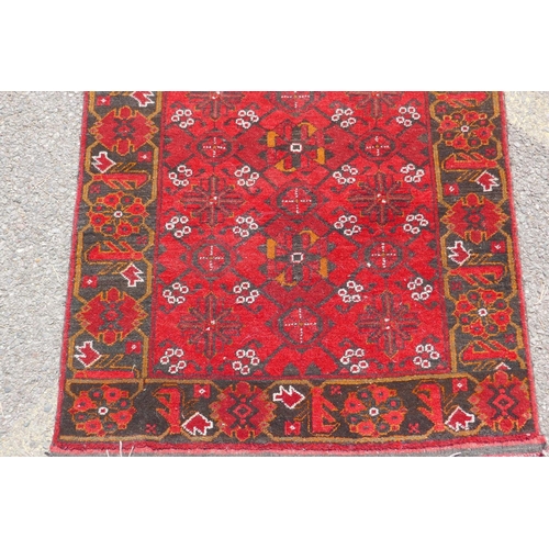 1227 - A Persian wool runner with geometric designs on a red field and black borders, 85 x 288cm