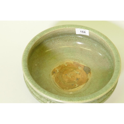 184 - An oriental crackle glazed green bowl with raised boss and low relief decoration, raised on tripod s... 