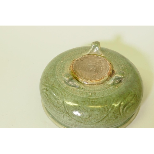 184 - An oriental crackle glazed green bowl with raised boss and low relief decoration, raised on tripod s... 