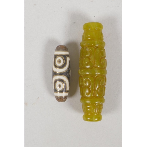 211 - A Tibetan brass inlaid Dzi bead and a carved green hardstone lozenge shaped bead, largest 6.5cm