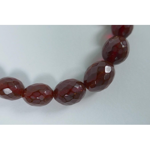 620 - A string of faceted and graduated cherry amber beads, 64g, 68cm, and a Baltic amber graduated bead n... 