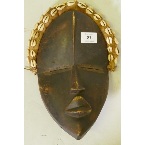 87 - African tribal mask, stained wood with textile headpiece inset with shells, Dan tribe, Ivory Coast, ... 