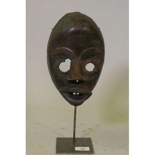 89 - African painted and carved wood tribal mask, Dan tribe, Ivory Coast, on a metal stand, 37cm