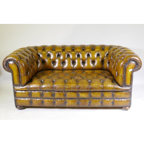 1003 - A leather chesterfield with button back and seat, and studded decoration, raised on bun feet, 177cm ... 