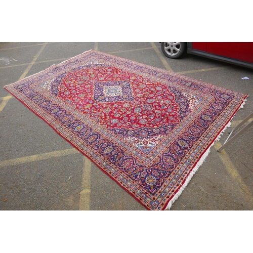 1031 - A red ground Kashan carpet with central blue medallion design and blue borders, 180 x 240cm