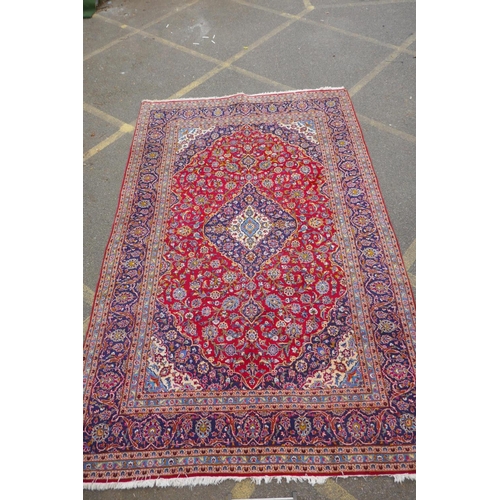 1031 - A red ground Kashan carpet with central blue medallion design and blue borders, 180 x 240cm