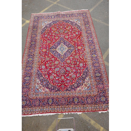 1031 - A red ground Kashan carpet with central blue medallion design and blue borders, 180 x 240cm