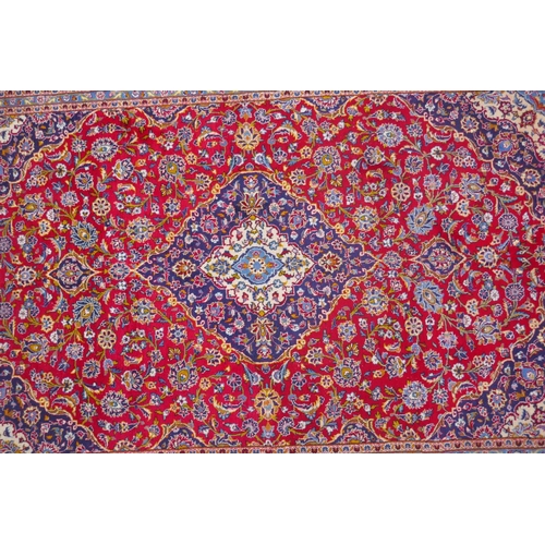 1031 - A red ground Kashan carpet with central blue medallion design and blue borders, 180 x 240cm