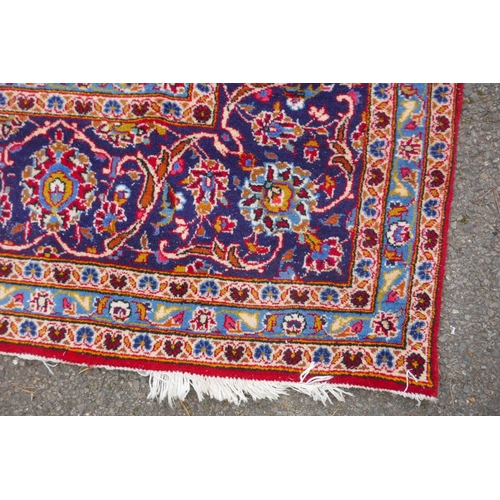 1031 - A red ground Kashan carpet with central blue medallion design and blue borders, 180 x 240cm