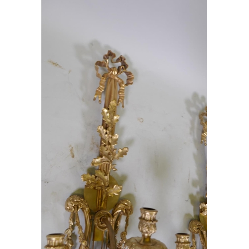 1056 - A pair of ormolu three branch Rococo style wall sconces with putti, oak leaf and swag decoration, 98... 