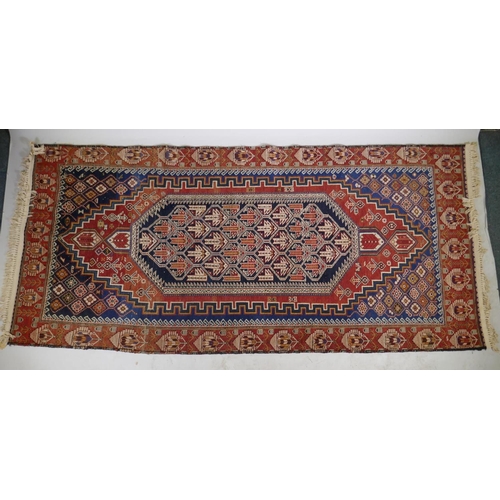 1060 - An antique Persian red ground wool Yalameh rug with a blue medallion design, 118 x 255cm