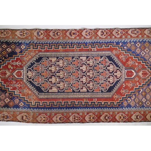 1060 - An antique Persian red ground wool Yalameh rug with a blue medallion design, 118 x 255cm