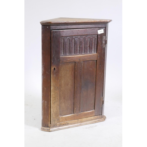 1070 - A small Arts & Crafts style oak hanging corner cupboard, the door with fielded panels and carved... 