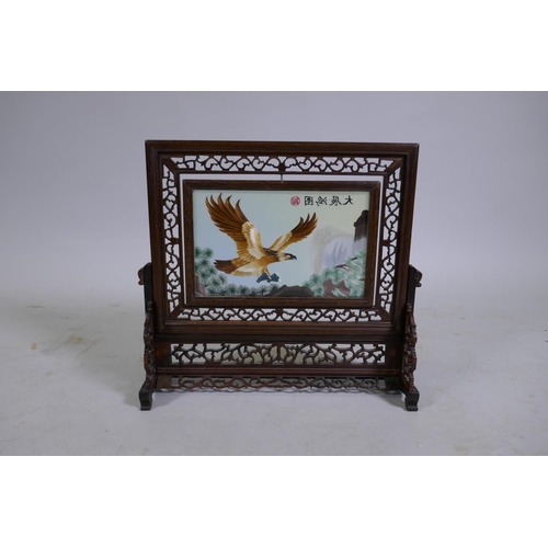 132 - A Chinese pierced hardwood table screen fitted with a revolving glazed embroidered silk panel depict... 