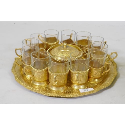 53 - A Middle Eastern gilt metal serving tray with fitted sugar bowl and twelve glass beakers with holder... 