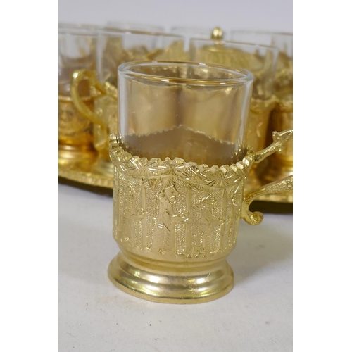 53 - A Middle Eastern gilt metal serving tray with fitted sugar bowl and twelve glass beakers with holder... 