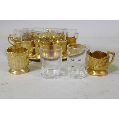 53 - A Middle Eastern gilt metal serving tray with fitted sugar bowl and twelve glass beakers with holder... 