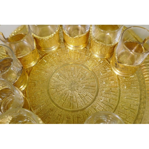 53 - A Middle Eastern gilt metal serving tray with fitted sugar bowl and twelve glass beakers with holder... 