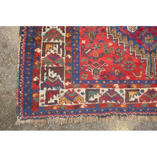 1093 - A C19th Persian red ground Qashqai tribal rug decorated with blue geometric medallion design, surrou... 