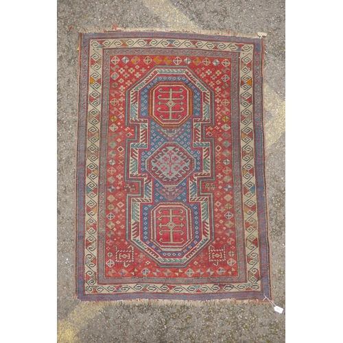 1100 - An antique red ground Kazak rug with blue and red medallion design, 100 x 140cm