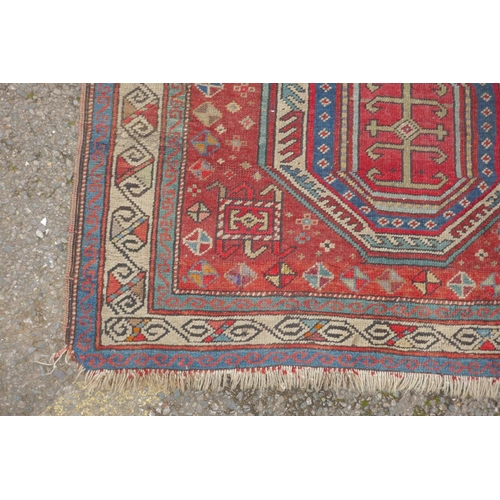 1100 - An antique red ground Kazak rug with blue and red medallion design, 100 x 140cm