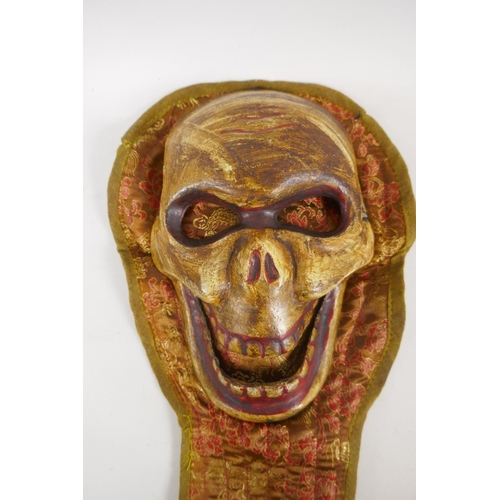 22 - A Tibetan painted metal Citipati death mask on an embroidered silk mount, 46cm