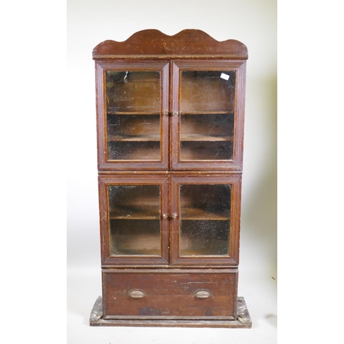 1151 - A C19th stained pine shop cabinet, two pairs of glazed doors over a single drawer, 87 x 29 x 153cm