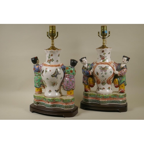 15 - A pair of ceramic table lamps in the form of a vase flanked by two boys, raised on a wood base, 46cm... 