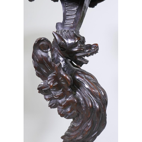 1001 - A pair of stained and carved pine stands in the form of griffins, raised on tripod supports, possibl... 