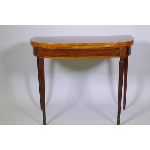 1007 - A Georgian mahogany D shaped card table, with cross banded top and frieze, raised on reeded tapering... 